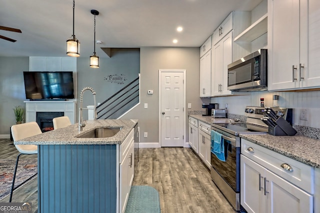 kitchen featuring wood finished floors, an island with sink, a sink, a lit fireplace, and stainless steel appliances