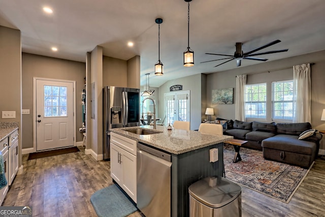 kitchen with light stone counters, a sink, dark wood-type flooring, appliances with stainless steel finishes, and decorative light fixtures