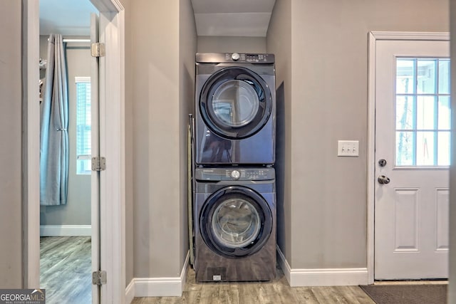 laundry room with laundry area, stacked washer / drying machine, baseboards, and wood finished floors