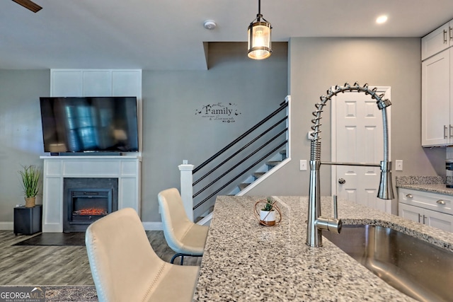 interior space featuring a sink, a glass covered fireplace, wood finished floors, white cabinetry, and light stone countertops