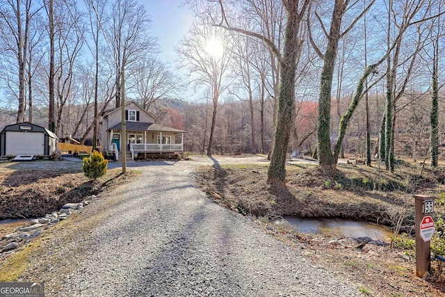 view of front facade featuring gravel driveway, an outbuilding, covered porch, and a wooded view