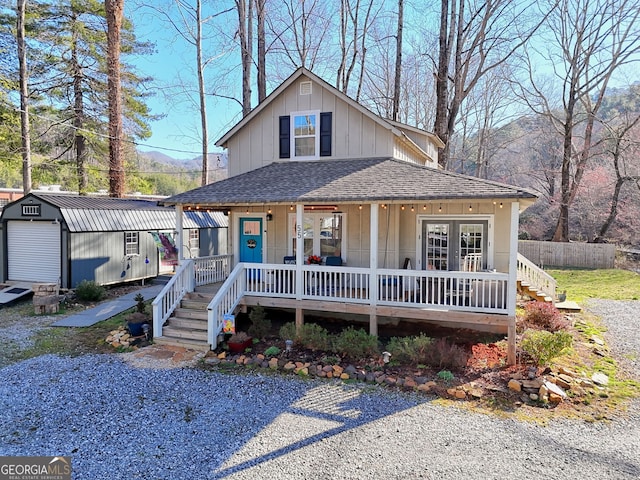 view of front of property with an outbuilding, a shed, roof with shingles, covered porch, and board and batten siding