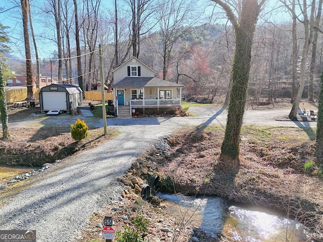 view of front facade with gravel driveway, a porch, an outdoor structure, and a storage shed