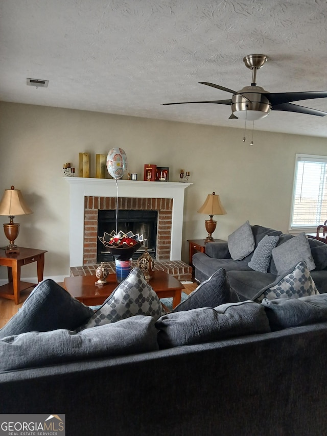 living area with visible vents, a ceiling fan, a textured ceiling, wood finished floors, and a brick fireplace