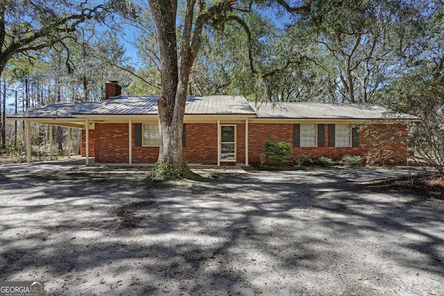 view of front of property featuring brick siding, an attached carport, driveway, and a chimney