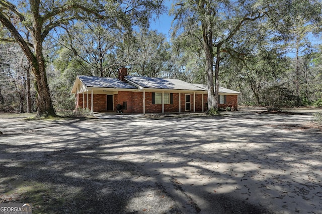 view of front facade featuring an attached carport, brick siding, driveway, and a chimney