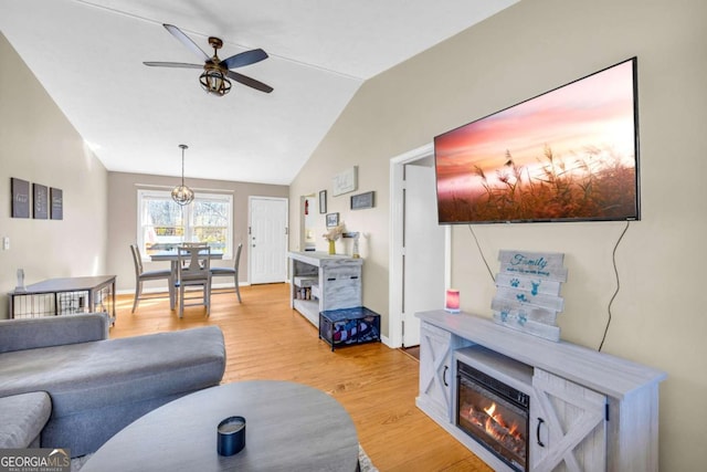 living area with a glass covered fireplace, light wood finished floors, baseboards, ceiling fan, and vaulted ceiling