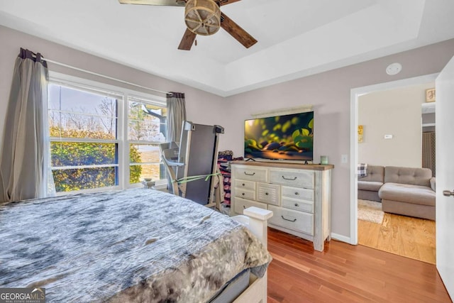 bedroom with baseboards, a raised ceiling, wood finished floors, and a ceiling fan