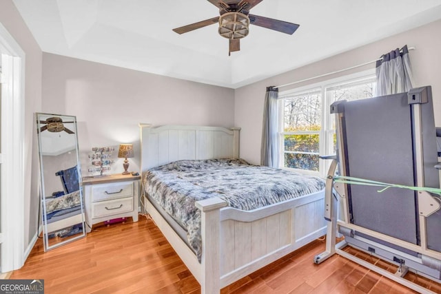 bedroom featuring a raised ceiling, light wood-style floors, and ceiling fan