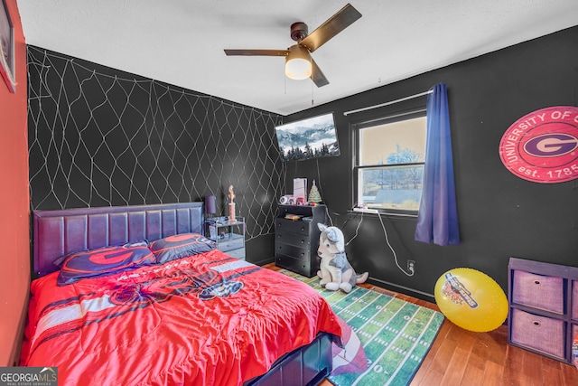 bedroom featuring baseboards, a ceiling fan, wood finished floors, and an accent wall