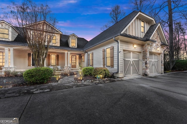 view of front facade with covered porch, a garage, stone siding, aphalt driveway, and board and batten siding