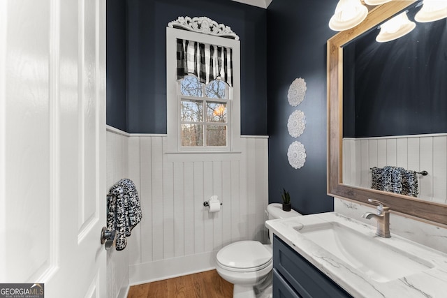 half bath featuring a wainscoted wall, toilet, vanity, and wood finished floors