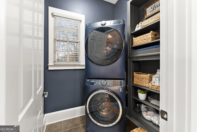 laundry room featuring baseboards, dark tile patterned floors, laundry area, and stacked washing maching and dryer