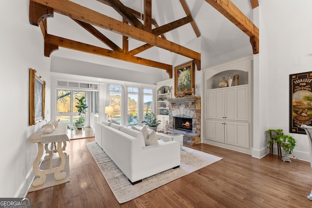 living room with wood finished floors, baseboards, high vaulted ceiling, a stone fireplace, and beamed ceiling