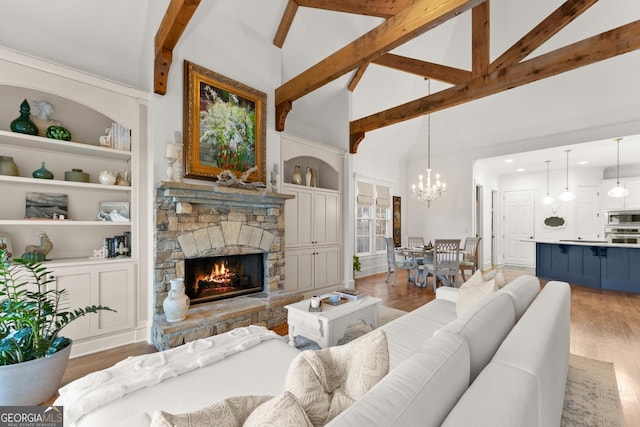 living room featuring a stone fireplace, beamed ceiling, built in shelves, and light wood-style floors