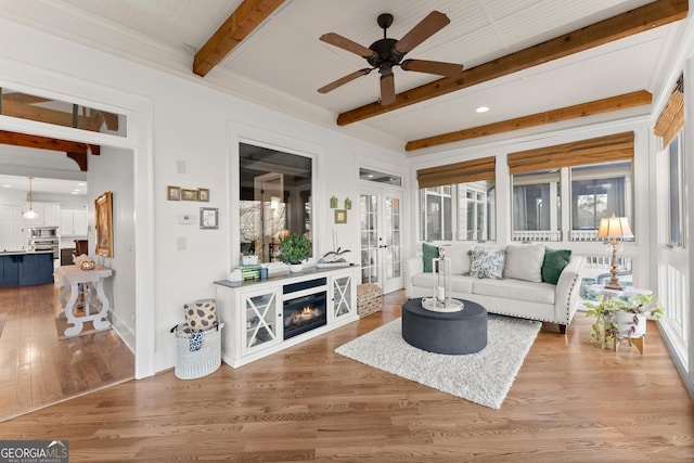 living room with a ceiling fan, beamed ceiling, wood finished floors, and french doors