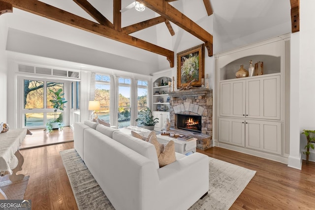 living room with a stone fireplace, beam ceiling, light wood-style flooring, and built in shelves