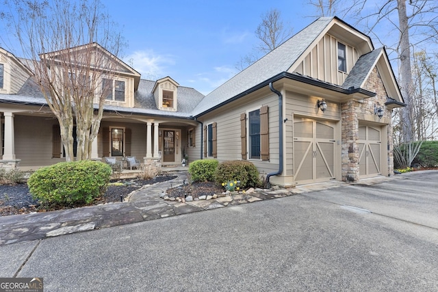 craftsman house with aphalt driveway, stone siding, covered porch, and board and batten siding