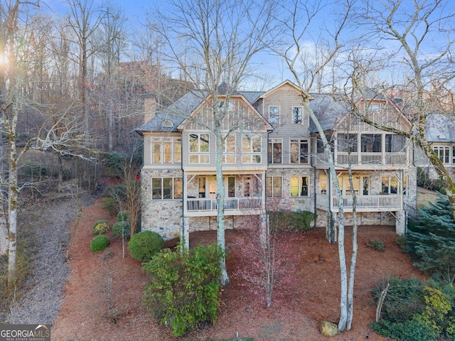 view of front of home featuring a balcony, covered porch, stone siding, and a chimney