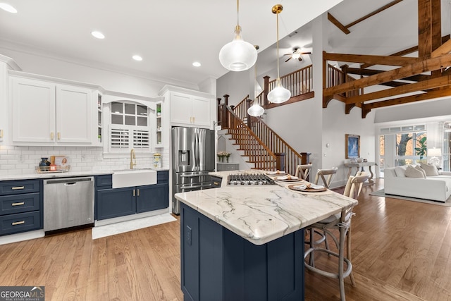 kitchen with light wood-type flooring, appliances with stainless steel finishes, white cabinetry, blue cabinets, and a sink