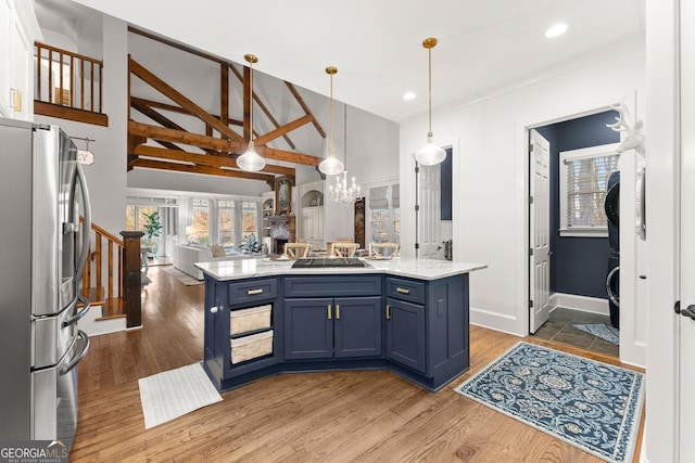 kitchen featuring gas cooktop, stainless steel refrigerator with ice dispenser, stacked washer and clothes dryer, blue cabinets, and open floor plan