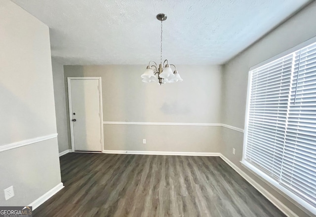 unfurnished dining area featuring baseboards, a textured ceiling, an inviting chandelier, and wood finished floors