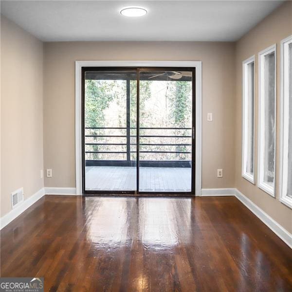 spare room with wood finished floors, visible vents, and baseboards