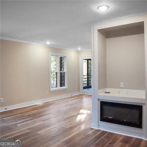 unfurnished living room featuring a glass covered fireplace, crown molding, baseboards, and wood finished floors