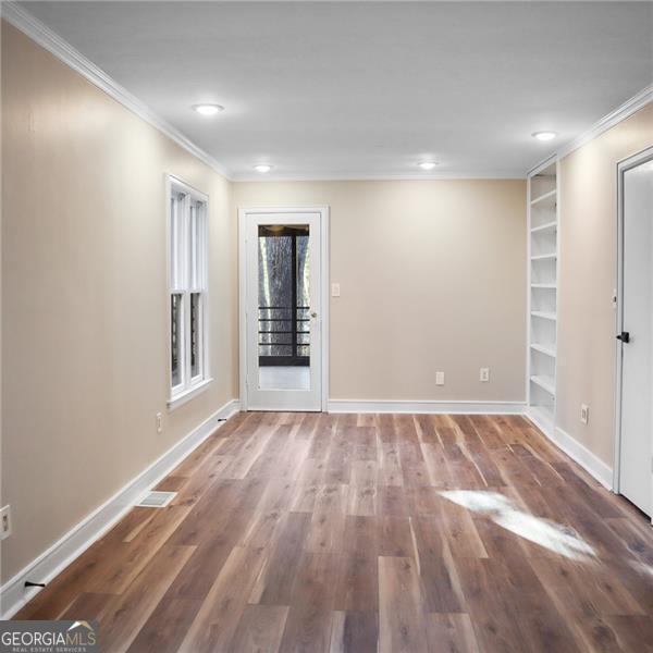 empty room with visible vents, built in shelves, wood finished floors, crown molding, and baseboards