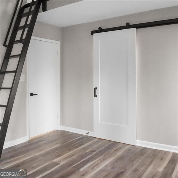 unfurnished bedroom featuring a barn door, wood finished floors, and baseboards