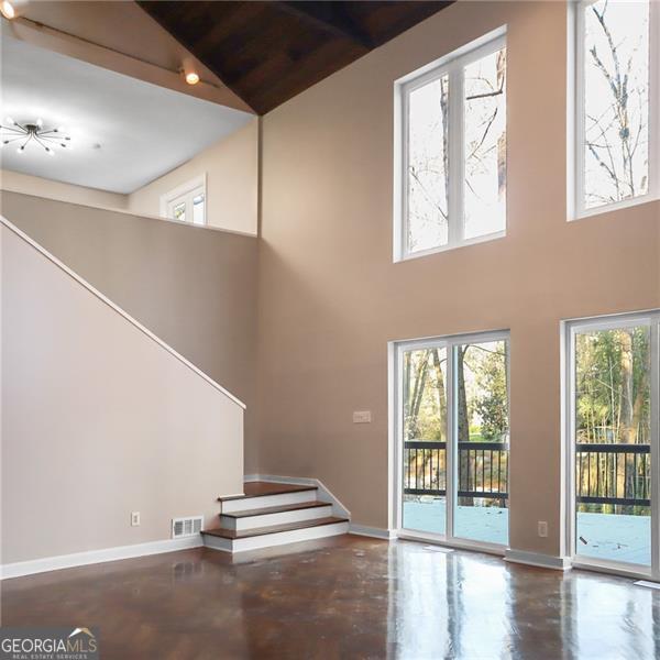 unfurnished living room with stairway, baseboards, visible vents, and high vaulted ceiling