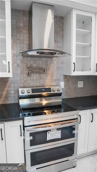 kitchen with dark countertops, glass insert cabinets, wall chimney exhaust hood, and range with two ovens