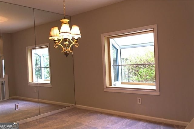 unfurnished dining area featuring an inviting chandelier, carpet flooring, and baseboards