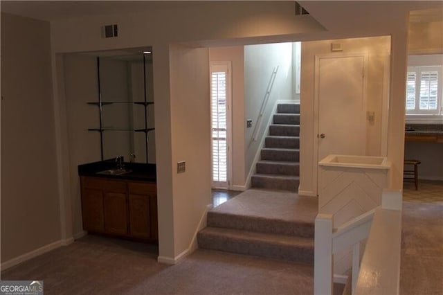 stairs with visible vents, wet bar, carpet, and baseboards