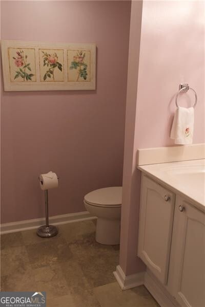 half bathroom featuring baseboards, toilet, and vanity