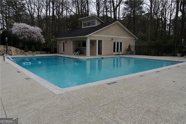 community pool with a patio area, fence, an outbuilding, and french doors