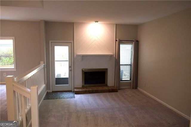 unfurnished living room with carpet flooring, a fireplace with raised hearth, baseboards, and a wealth of natural light