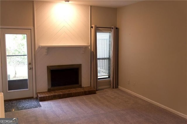 unfurnished living room with a glass covered fireplace, carpet flooring, baseboards, and a healthy amount of sunlight