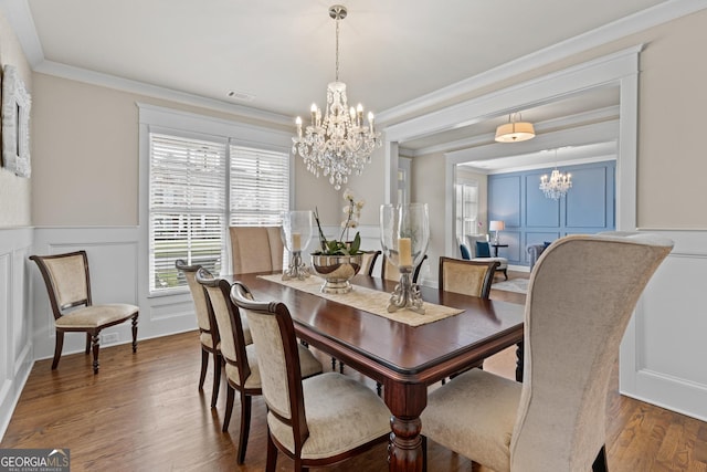 dining space with an inviting chandelier, wood finished floors, ornamental molding, and a decorative wall