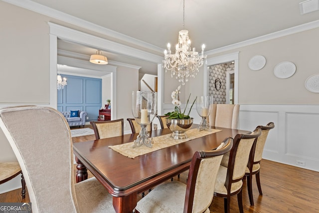 dining space with visible vents, a notable chandelier, wood finished floors, and a decorative wall