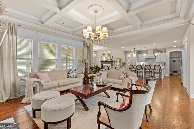 living area featuring light wood finished floors, coffered ceiling, a fireplace, and an inviting chandelier