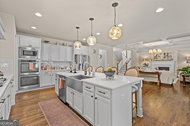 kitchen featuring a breakfast bar area, coffered ceiling, an island with sink, stainless steel appliances, and a sink