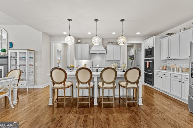 kitchen with stainless steel microwave, a kitchen breakfast bar, an island with sink, and wood finished floors