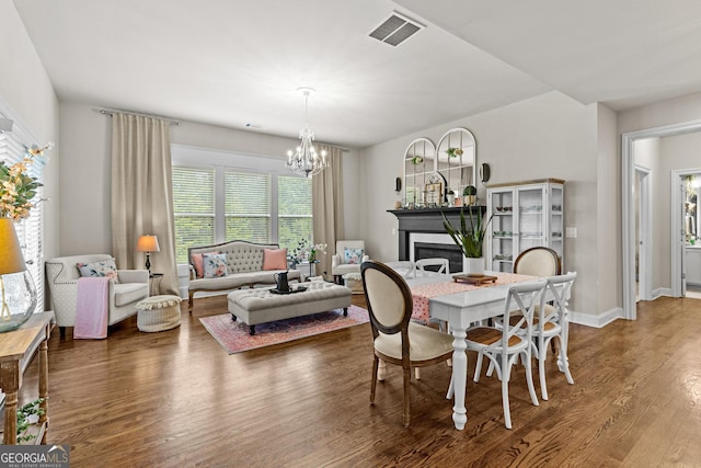 dining room featuring visible vents, baseboards, a chandelier, wood finished floors, and a glass covered fireplace