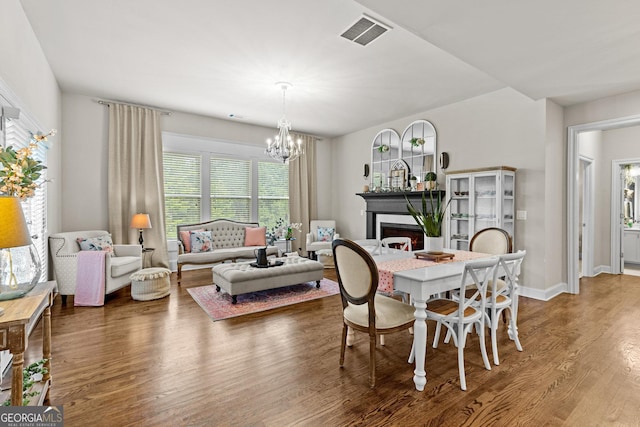 dining room with visible vents, a warm lit fireplace, wood finished floors, baseboards, and a chandelier