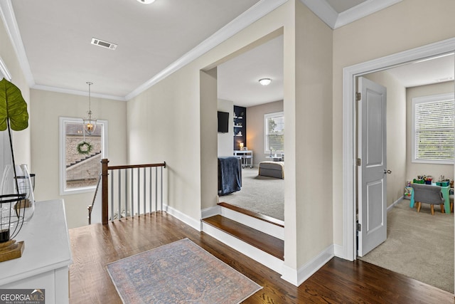 hallway featuring wood finished floors, baseboards, visible vents, ornamental molding, and an upstairs landing