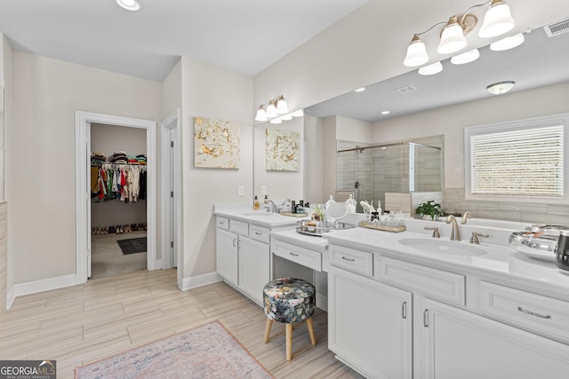 bathroom with visible vents, a shower stall, a walk in closet, baseboards, and vanity