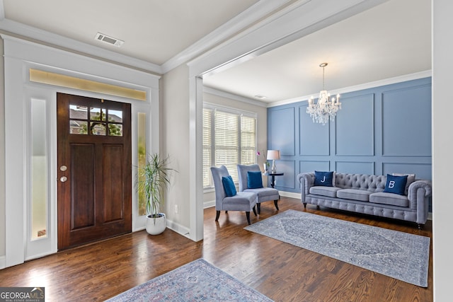 foyer featuring a notable chandelier, a decorative wall, crown molding, and dark wood-style floors