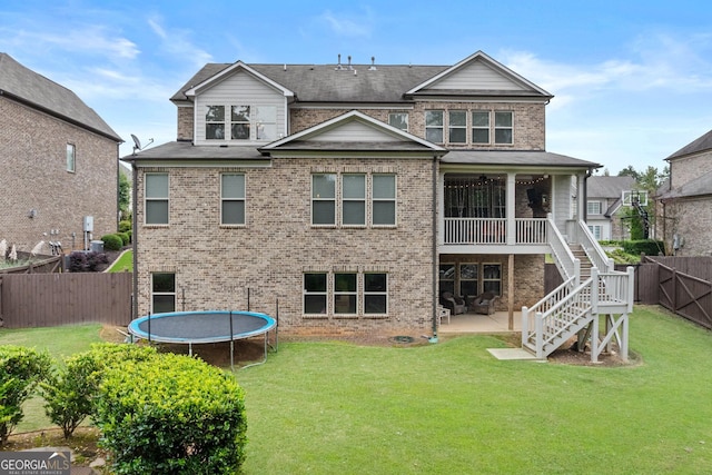 rear view of property with stairs, a lawn, a trampoline, a patio area, and brick siding