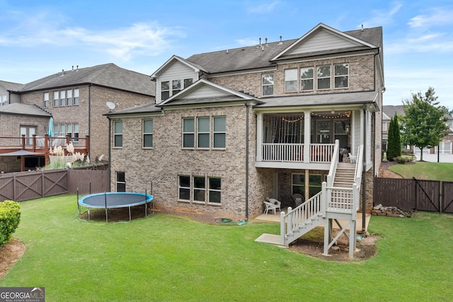 back of house with brick siding, stairway, a lawn, and a trampoline